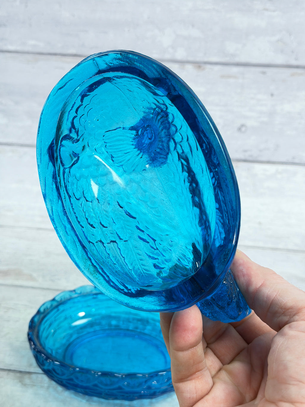 Blue glass hen-shaped lid topper for covered candy dish, held up