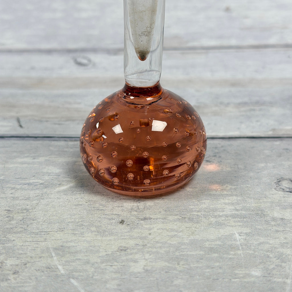 Close-up of rose-amber rounded base with controlled bubbles and visible residue inside the clear neck