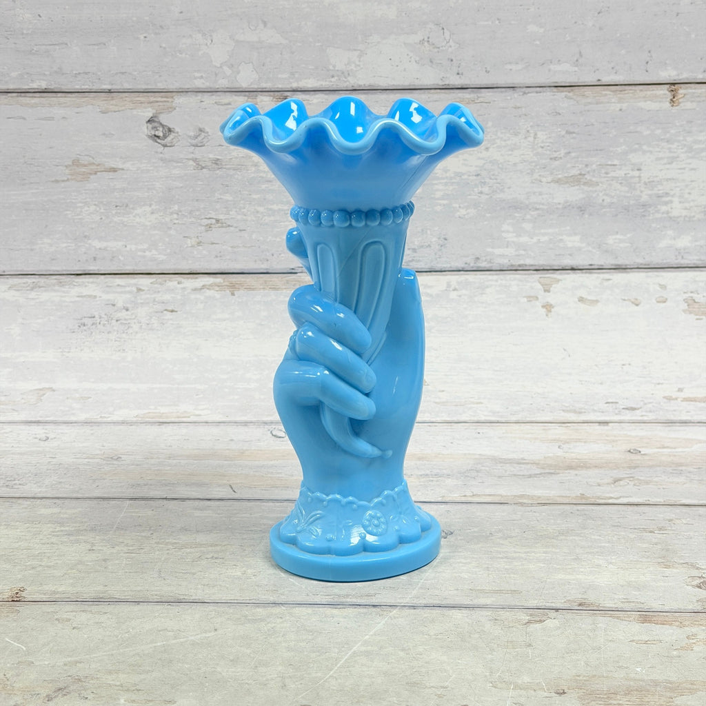 Opaque blue glass hand holding a cornucopia vase with ruffled rim