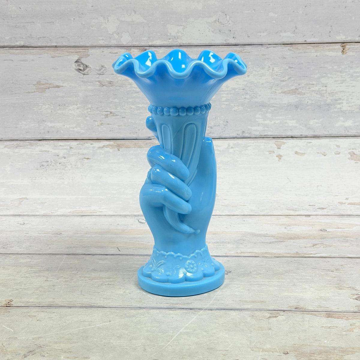 Opaque blue glass hand holding a cornucopia vase with ruffled rim
