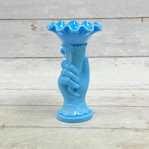 Opaque blue glass hand holding a cornucopia vase with ruffled rim