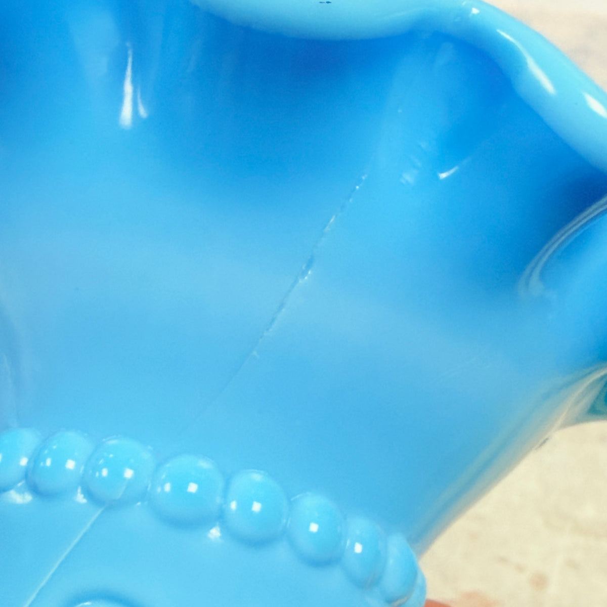 Close-up of hairline crack in upper flared section of blue glass hand vase