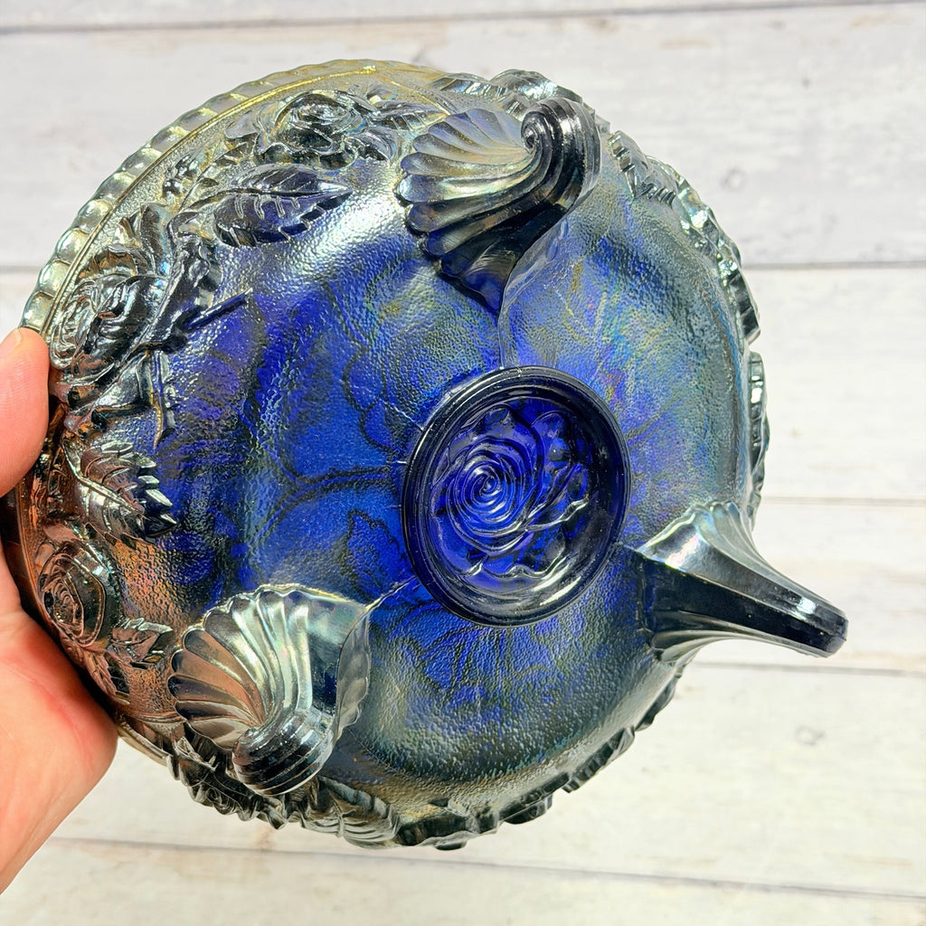 Underside of cobalt carnival glass rose-pattern bowl showing three scroll feet