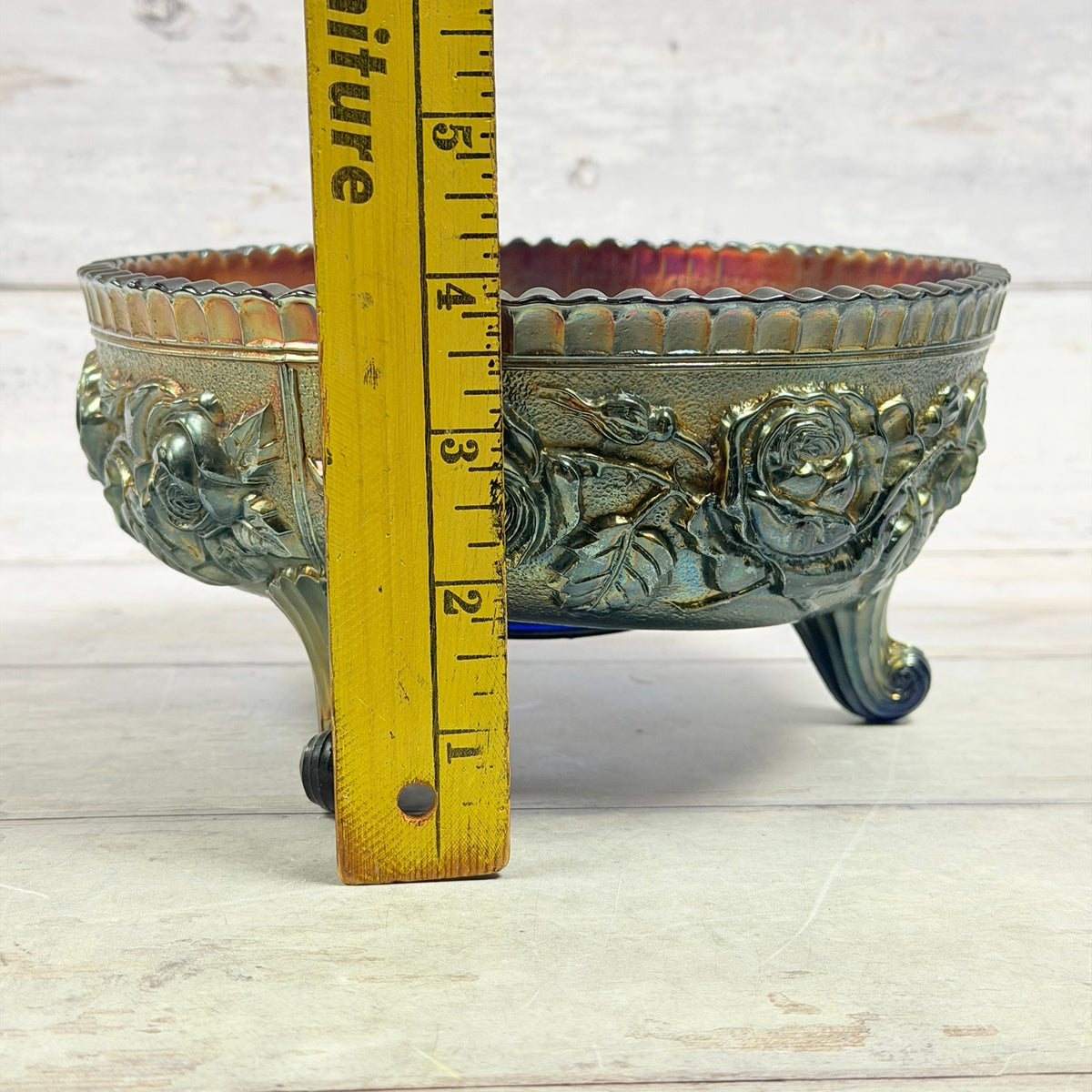 Side of cobalt carnival glass bowl with ruler showing height and scroll feet