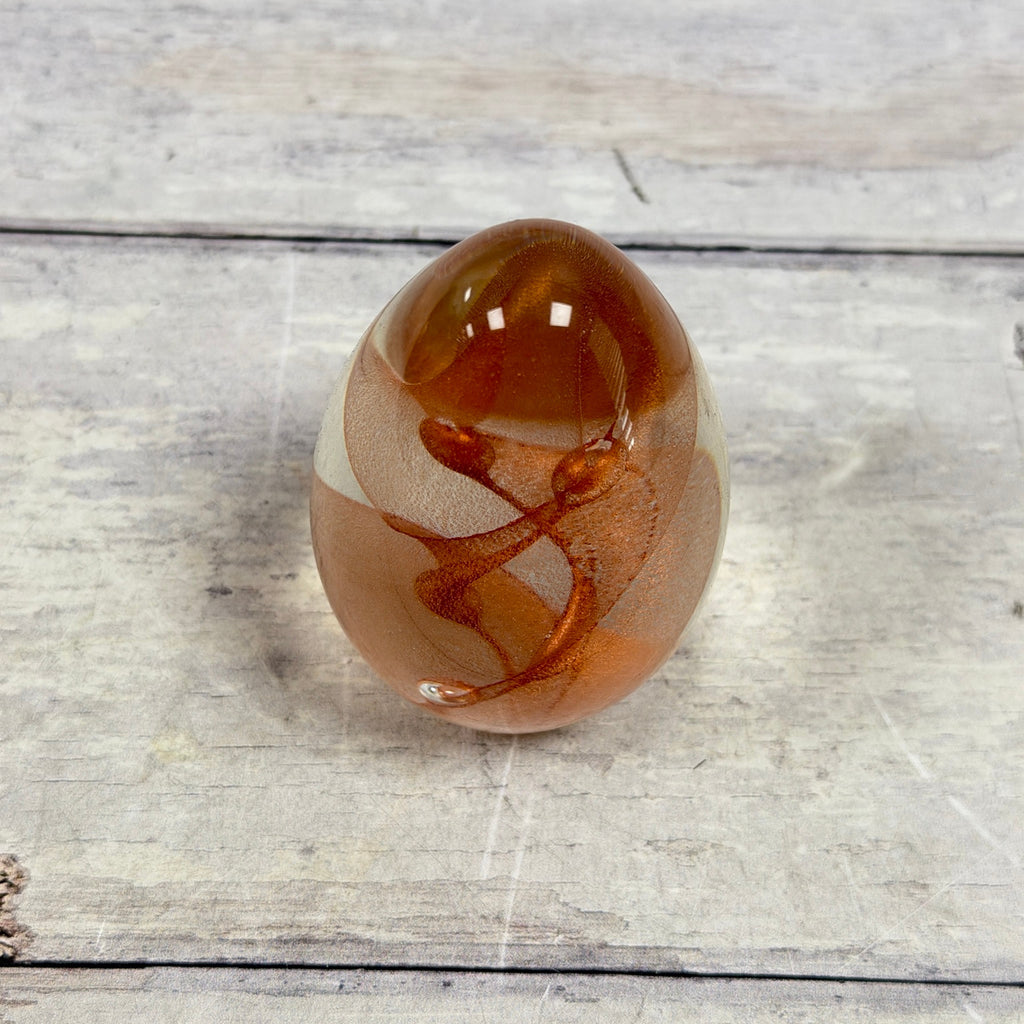Angled view of copper-toned spiral ribbons and a suspended bubble inside the glass egg