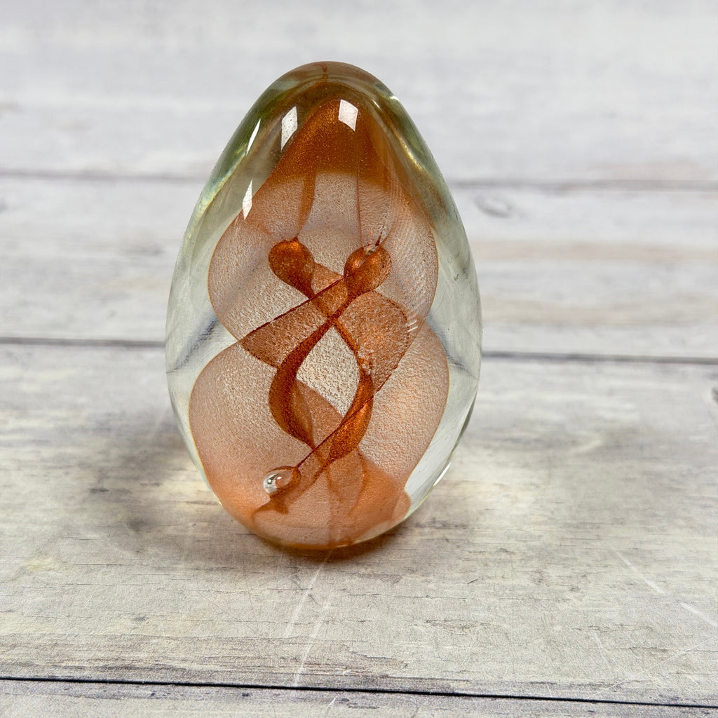 Copper and salmon ribbon swirls inside a clear egg-shaped art glass paperweight