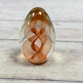 Copper and salmon ribbon swirls inside a clear egg-shaped art glass paperweight