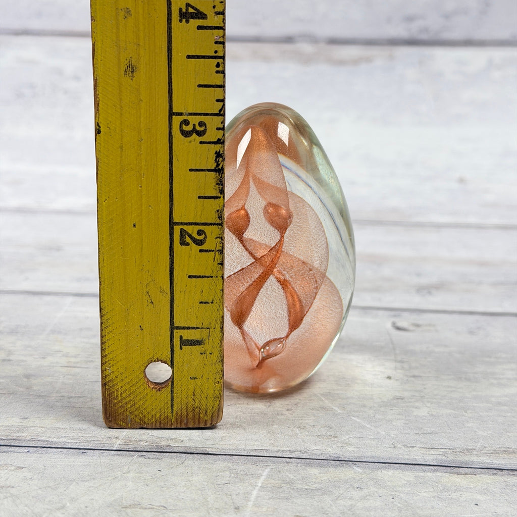 Copper ribbon glass egg paperweight beside a ruler showing an approximate three-inch height