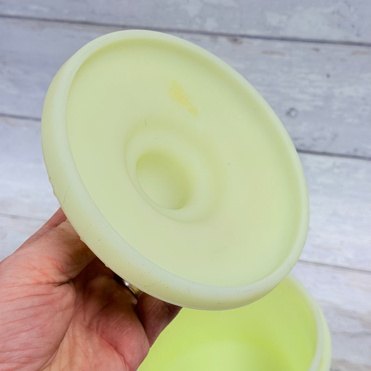 Underside of custard satin glass jar lid showing surface marks and a small discolored spot