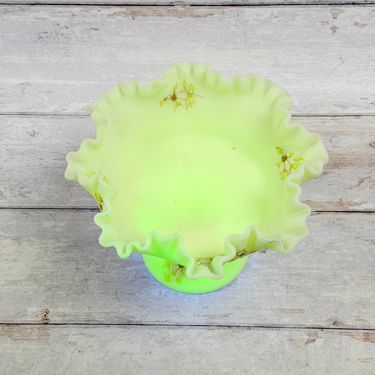 Top view of the Fenton daisy compote with a green ultraviolet glow across the bowl and pedestal