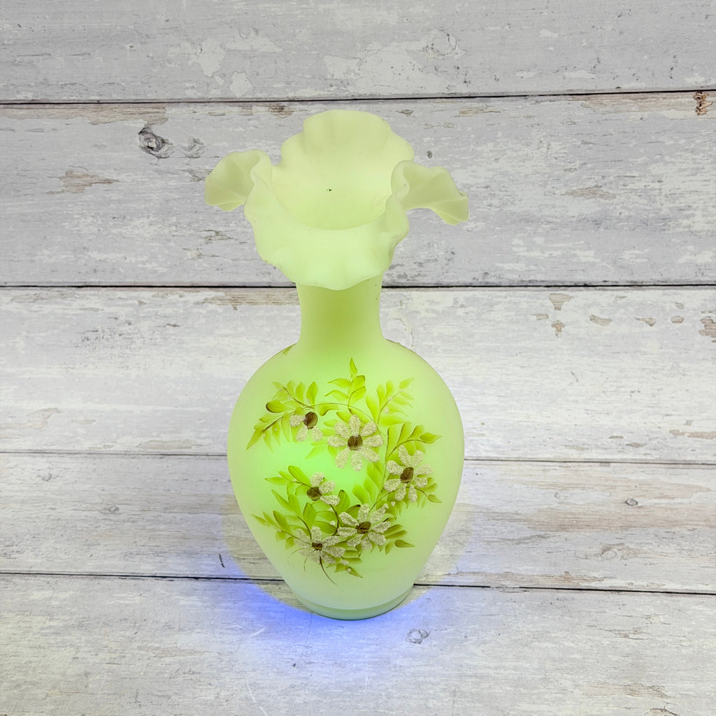 Upper view of Fenton custard uranium glass tall vase under UV light, showing the ruffled rim and small interior marks