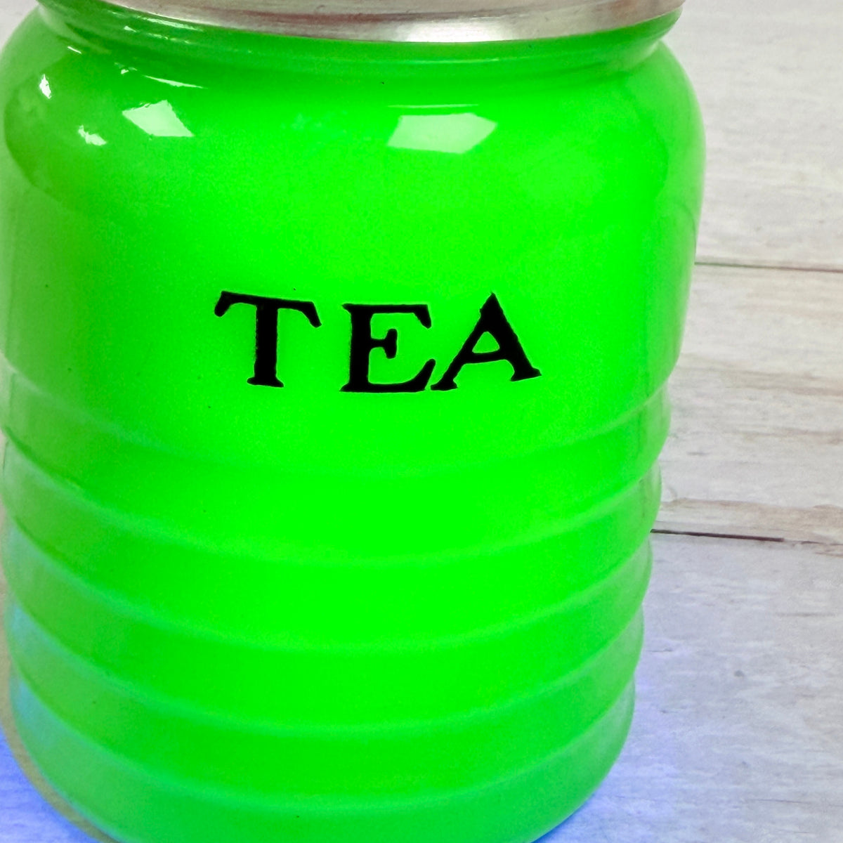 Close-up of black TEA lettering and bright green UV fluorescence on Jeannette canister J02