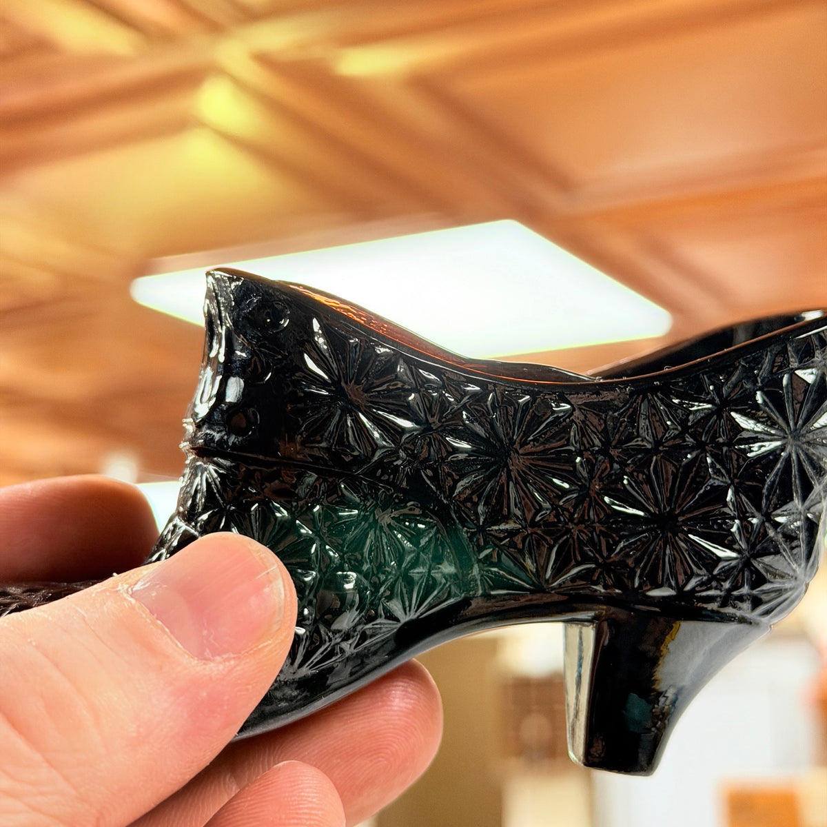 Close-up of black amethyst glass shoe held toward light showing pressed pattern and dark translucent color