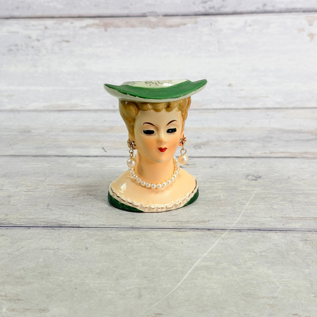 Front of small green hat head vase with pearl-style jewelry