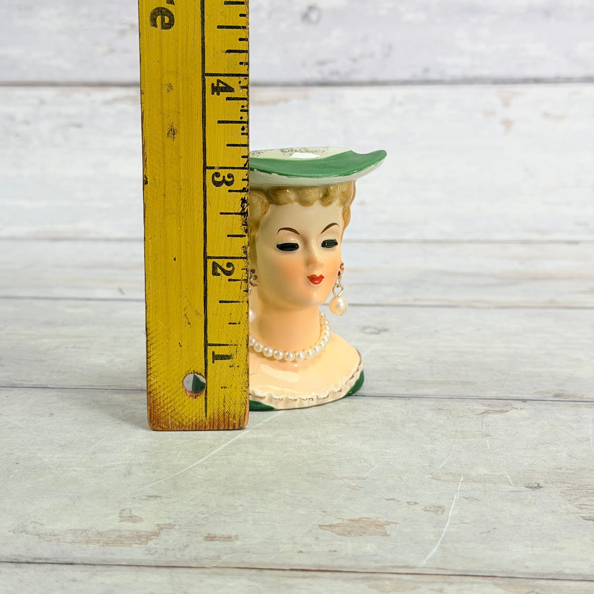 Small green hat vase beside ruler