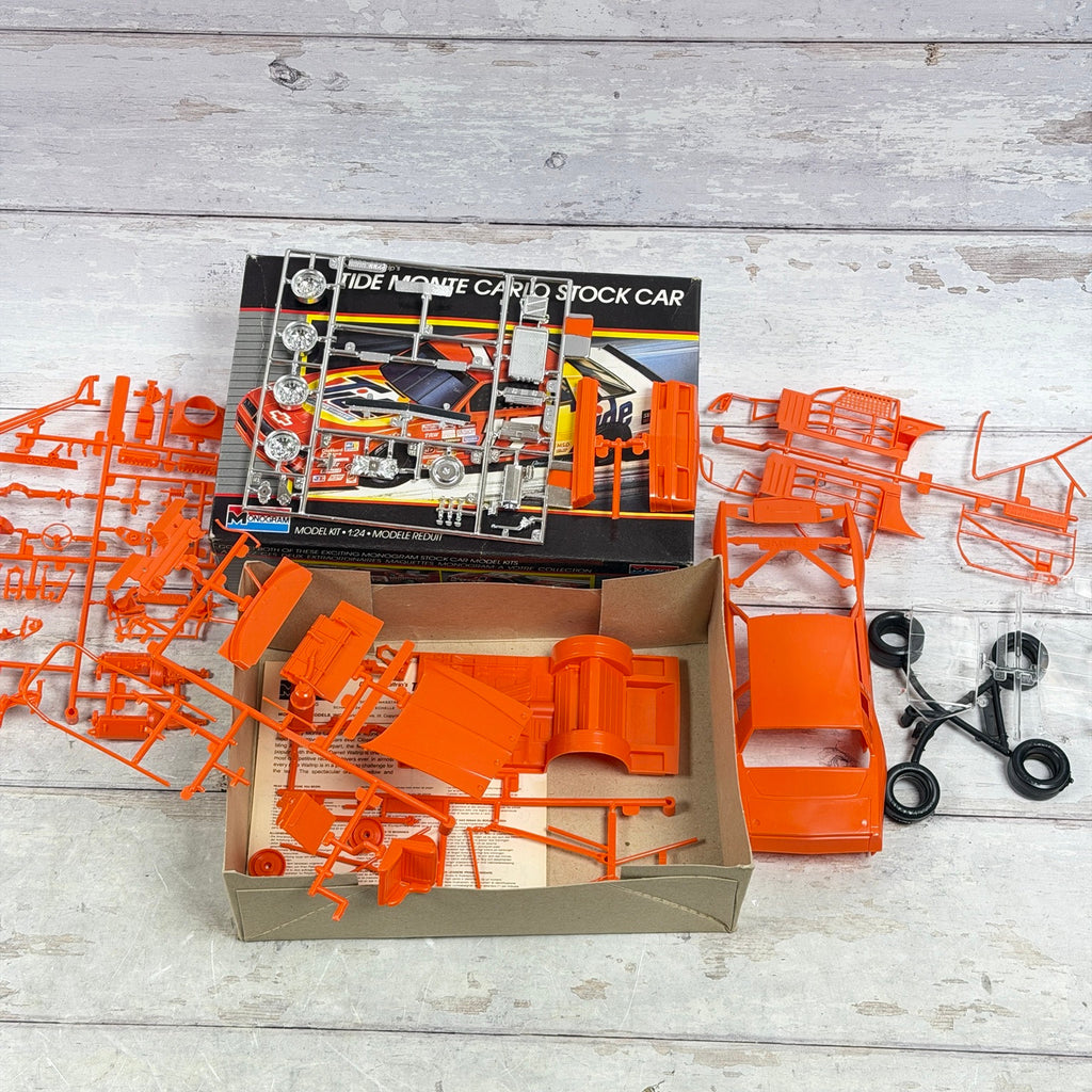 Unassembled orange parts, chrome and clear pieces, tires and instructions of Monogram 2755 Tide Monte Carlo kit