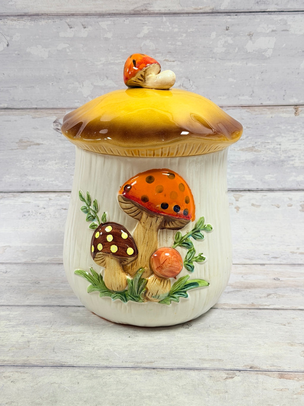 Front view of cream ceramic mushroom canister with yellow and brown lid, mushroom finial, and raised mushrooms