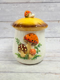 Front view of cream ceramic mushroom canister with yellow and brown lid, mushroom finial, and raised mushrooms