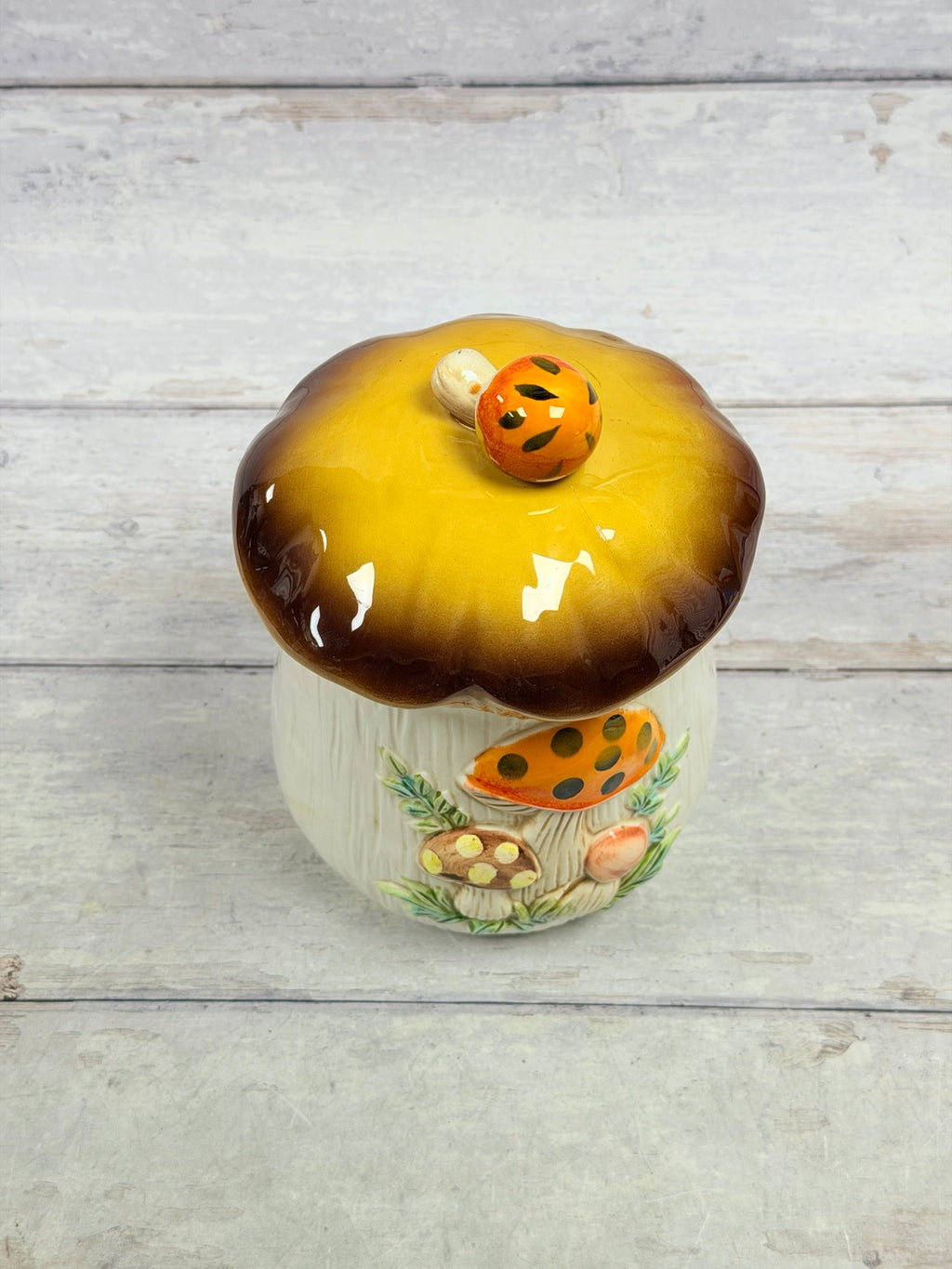 Front of Sears Merry Mushroom ceramic canister with raised mushrooms and brown-gold lid