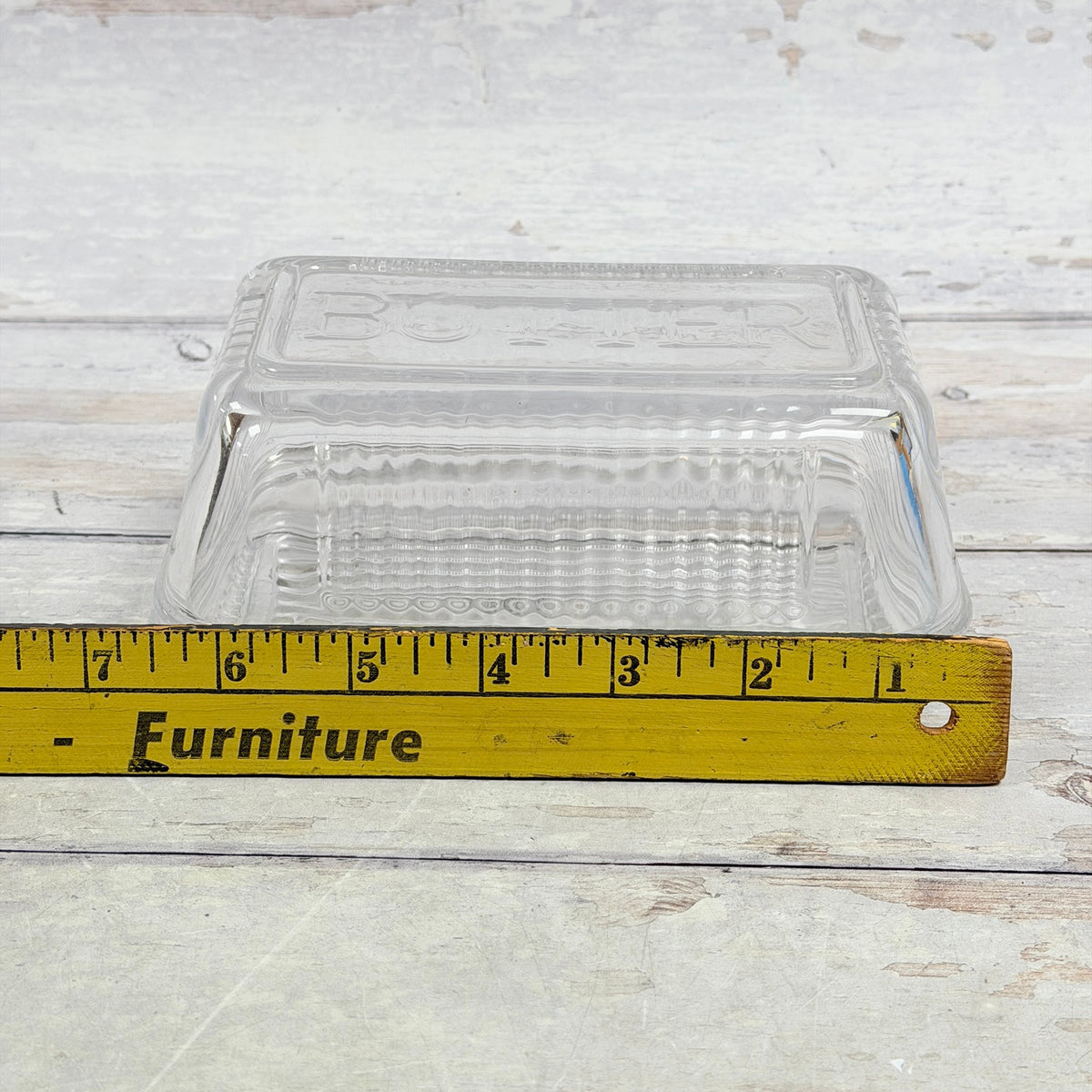 Clear glass covered butter dish beside ruler for size reference