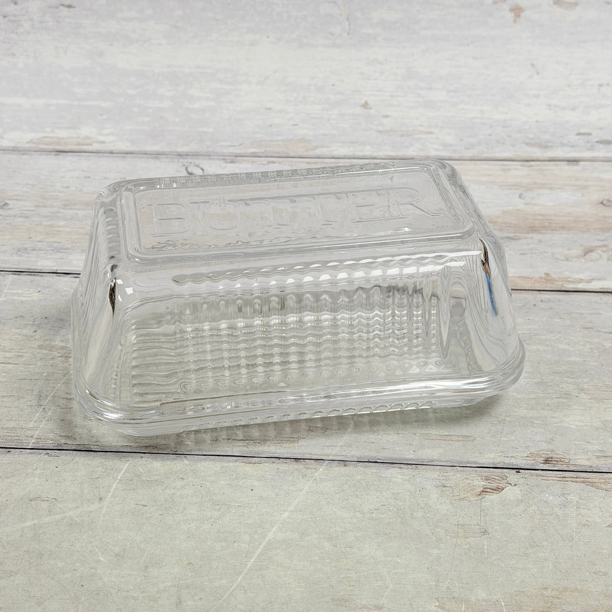 Clear ribbed glass butter dish with embossed BUTTER lid, front view
