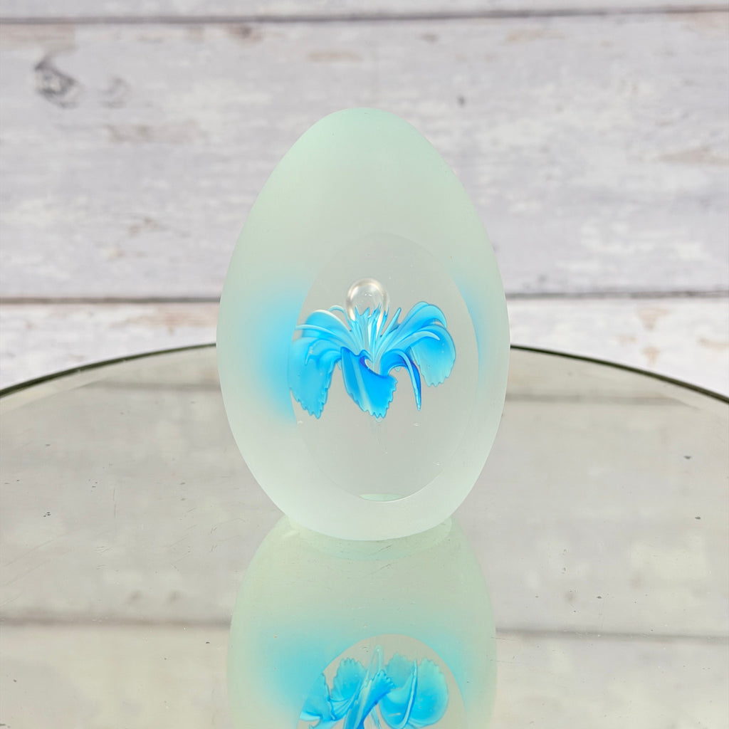 Frosted egg-shaped glass paperweight with blue flower and clear viewing window