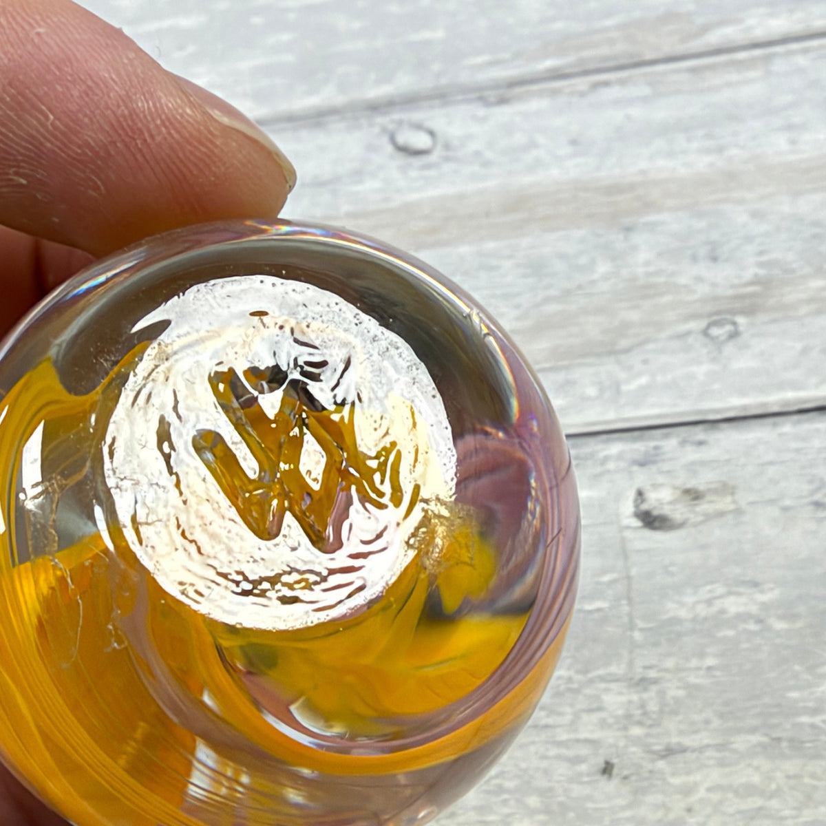 Underside of yellow and pink glass egg paperweight showing rough circular pontil area