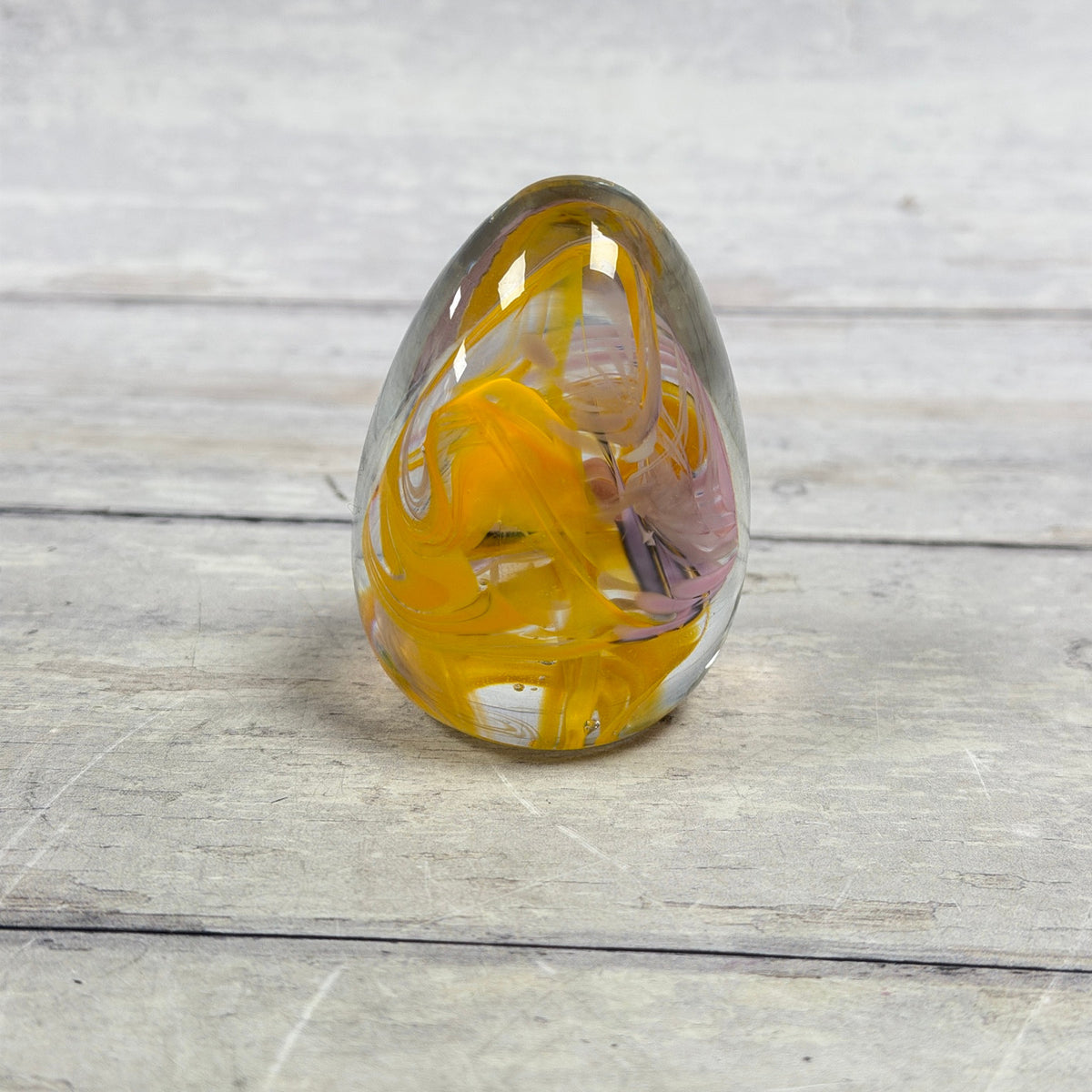 Clear glass egg paperweight with golden yellow and pale pink ribbon swirls