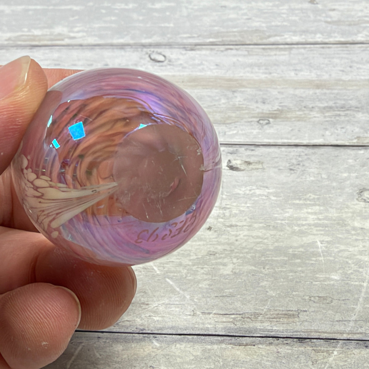 Base of Glass Eye Studio pink egg paperweight showing GES 93 inscription, scratches, and small edge nicks