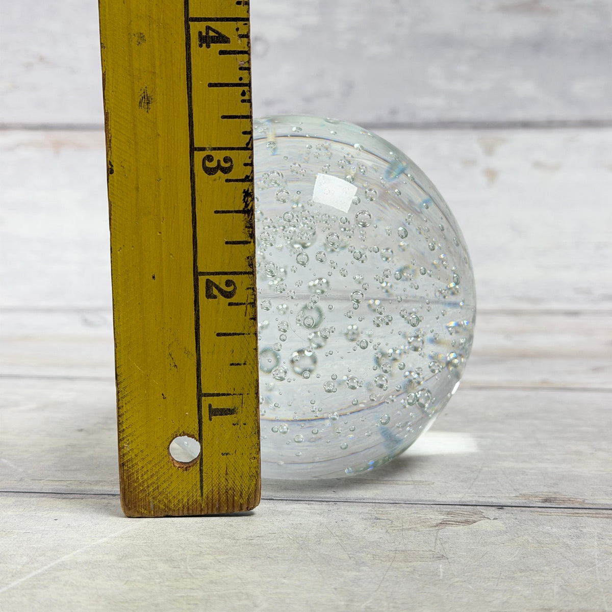 Clear bubble glass paperweight beside ruler for approximate height
