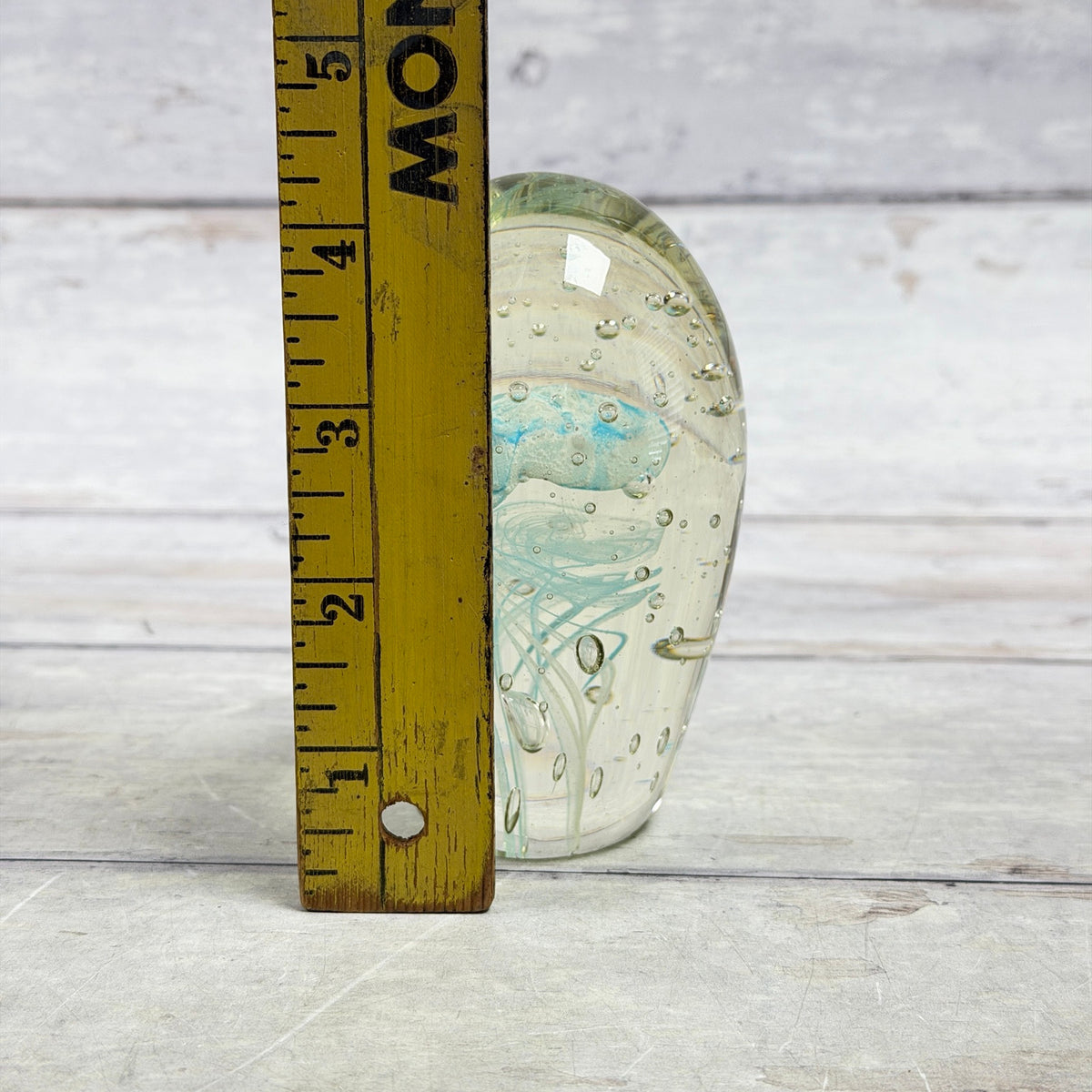 Blue jellyfish glass paperweight beside a wooden ruler showing its approximate four-inch height