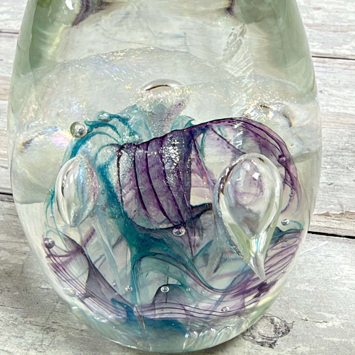 Close-up of teal and purple ribbons, fine shimmering veil and teardrop-shaped bubbles inside the clear glass