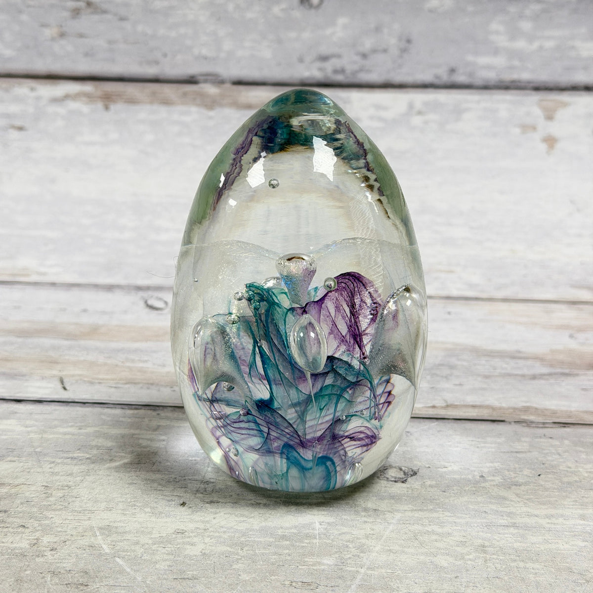 Egg-shaped art glass paperweight with teal and purple ribbons, a shimmering veil and controlled air bubbles