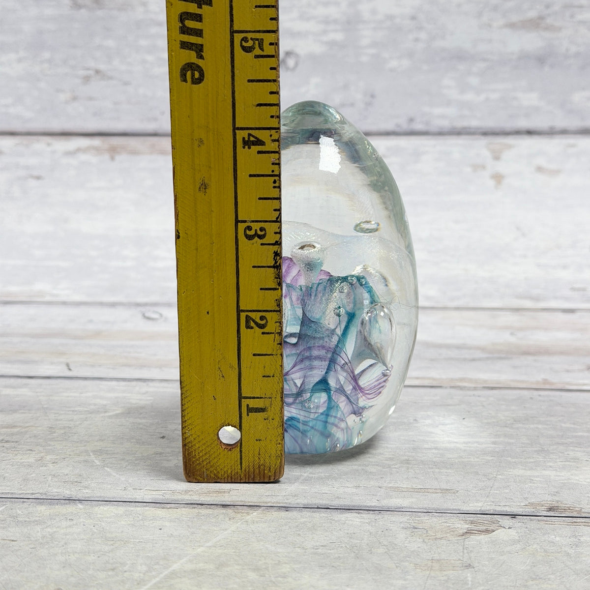 Ribbon and bubble glass egg paperweight beside a ruler showing approximately four and one-quarter inches tall