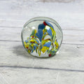 Rounded clear glass paperweight with blue, yellow, green, white and red confetti glass and controlled bubbles