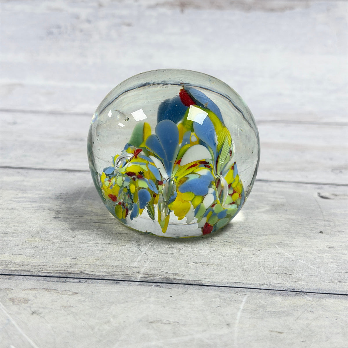 Rounded clear glass paperweight with blue, yellow, green, white and red confetti glass and controlled bubbles
