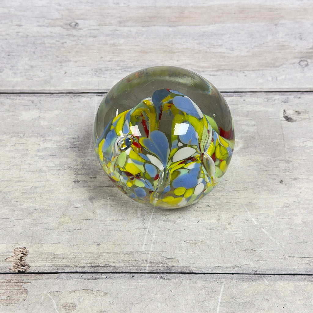 Angled top view of blue, yellow, green, white and red confetti patterns inside a clear glass paperweight