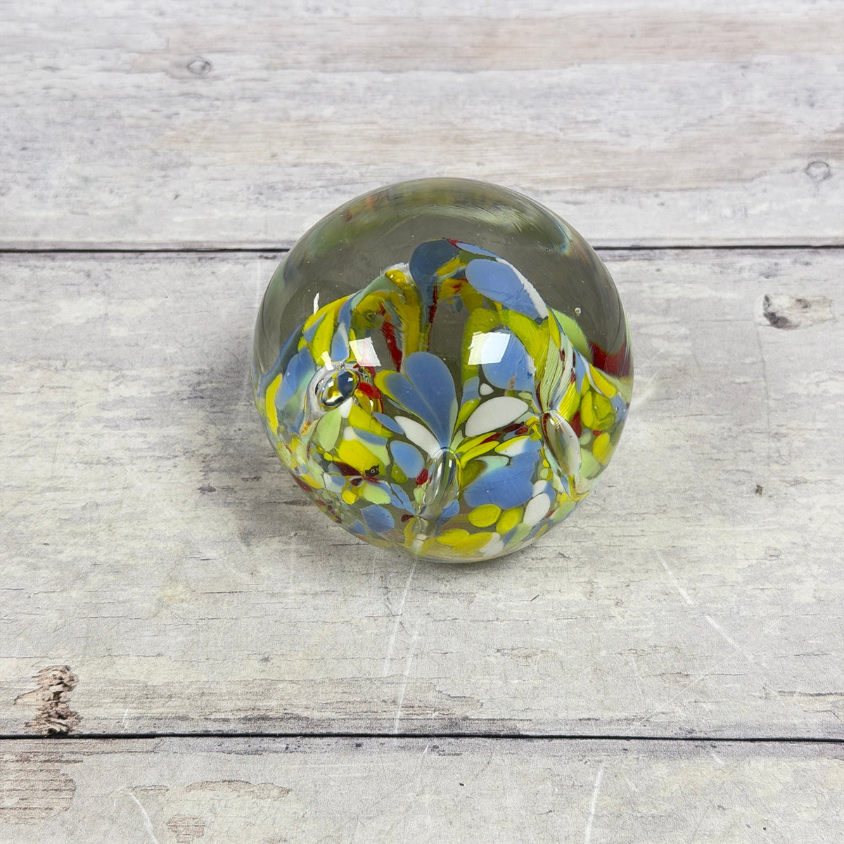 Angled top view of blue, yellow, green, white and red confetti patterns inside a clear glass paperweight
