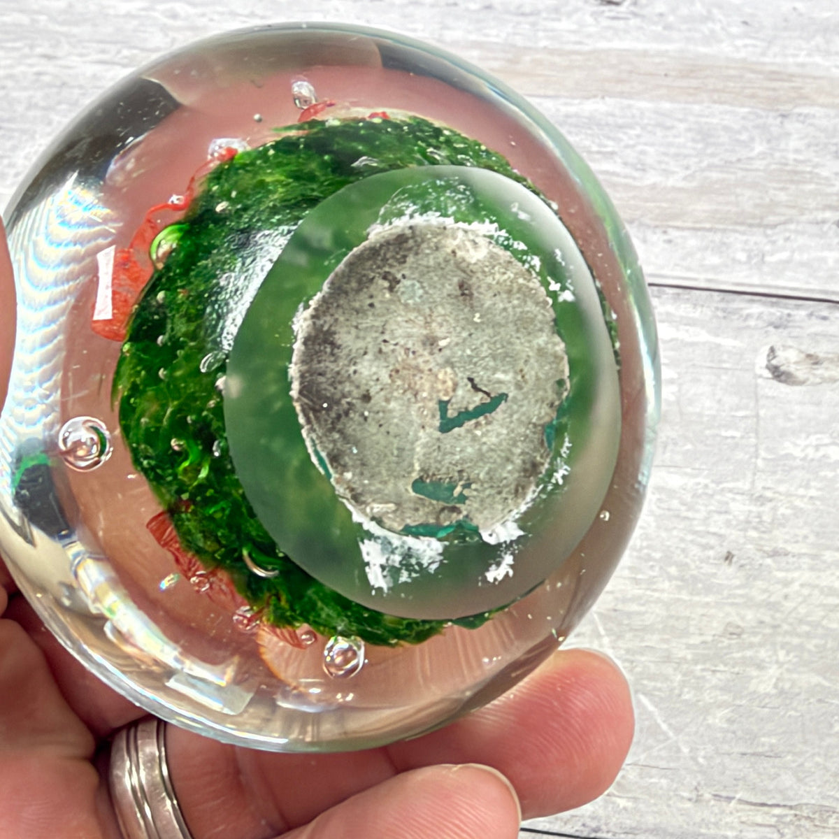 Underside of the glass paperweight showing a flat base, surface wear and an unreadable worn label