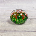 Clear glass paperweight with an orange-red ribbon flower, emerald green base and suspended air bubbles