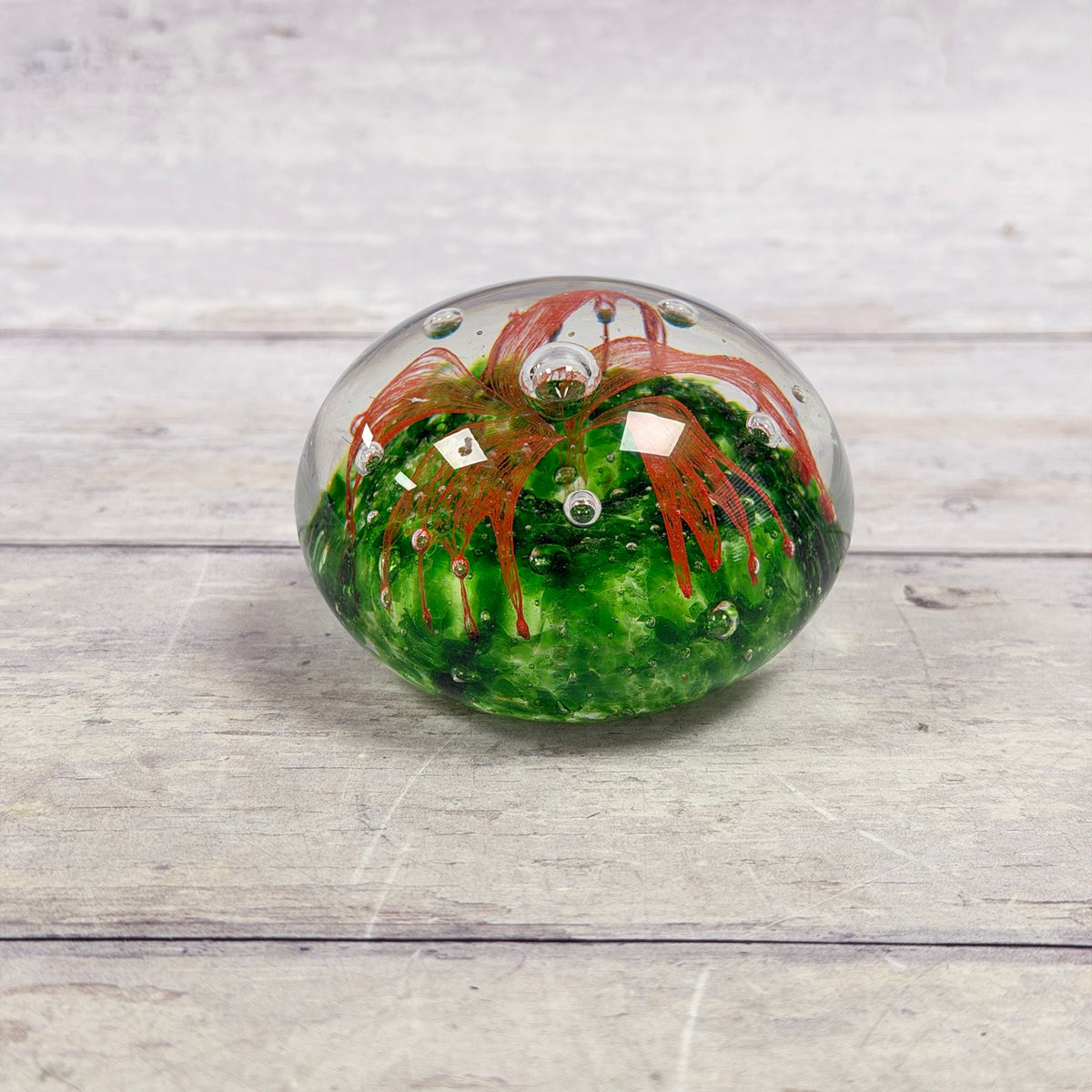 Clear glass paperweight with an orange-red ribbon flower, emerald green base and suspended air bubbles