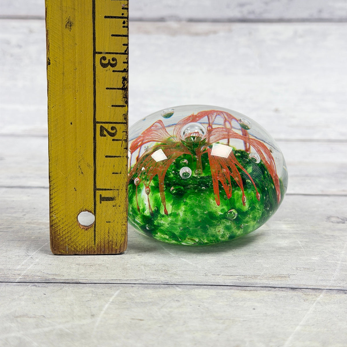 Orange flower and green glass paperweight beside a ruler showing an approximate two-and-a-quarter-inch height