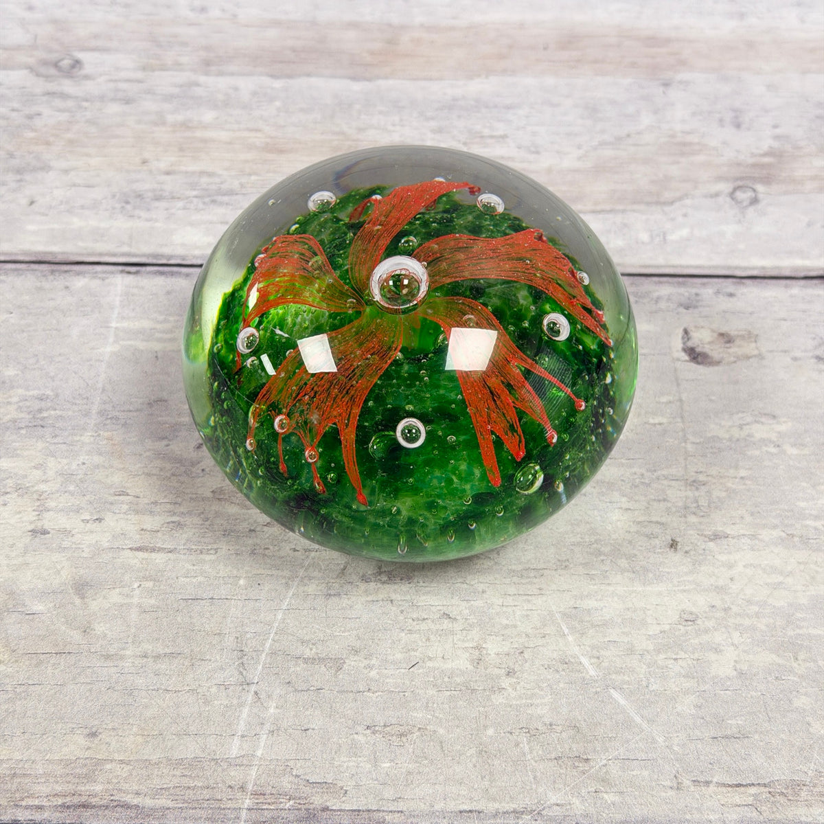 Top view of orange-red pinwheel-like flower and controlled bubbles over a mottled green glass base