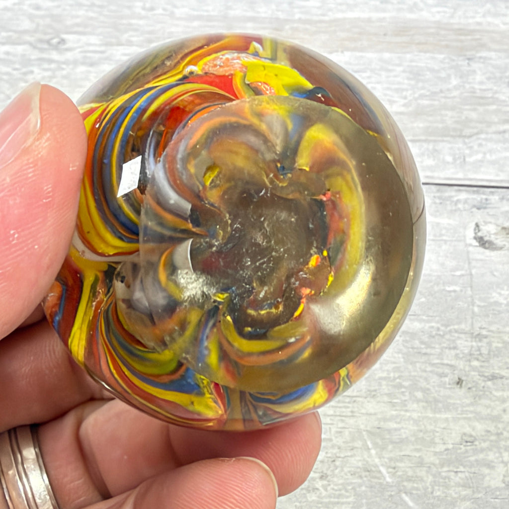 Underside of unsigned multicolor swirl glass paperweight showing flat base, wear and small rough marks