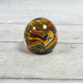 Egg-shaped clear glass paperweight with densely layered yellow, red, orange, blue, white and dark swirls