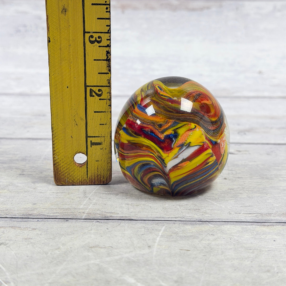 Multicolor swirl art glass egg paperweight beside a ruler showing an approximate two-and-a-quarter-inch height