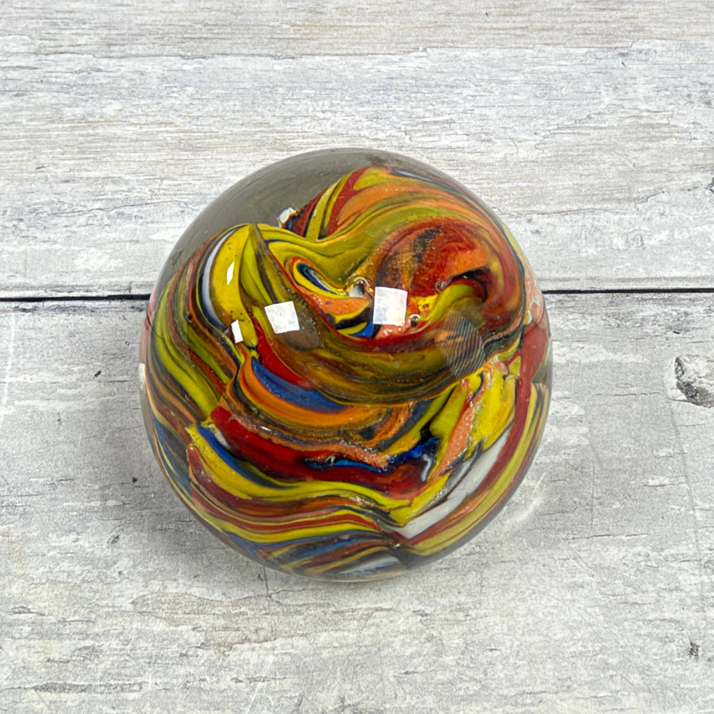 Angled top view of a multicolor swirl glass egg paperweight showing bands of yellow, red, blue and orange