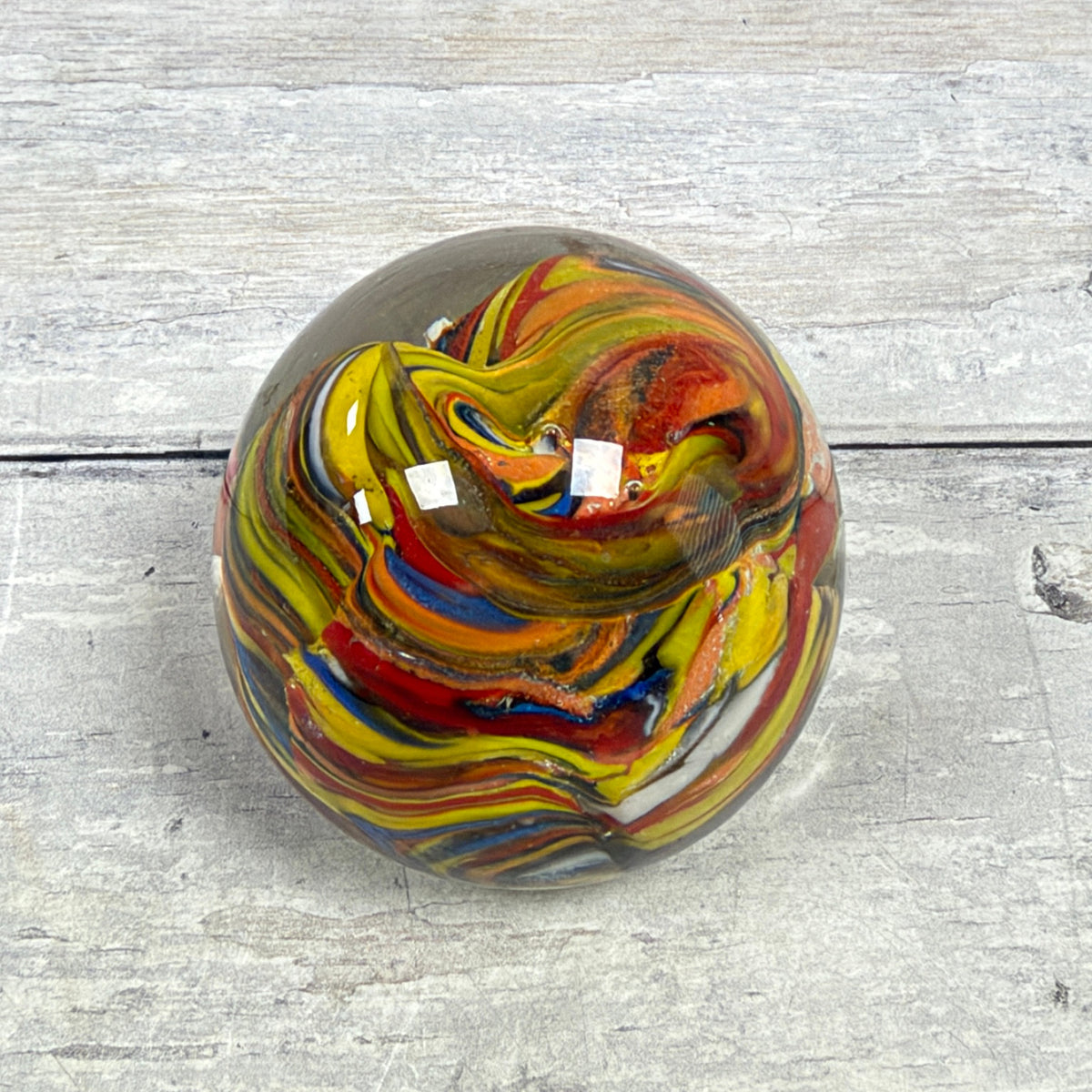 Angled top view of a multicolor swirl glass egg paperweight showing bands of yellow, red, blue and orange