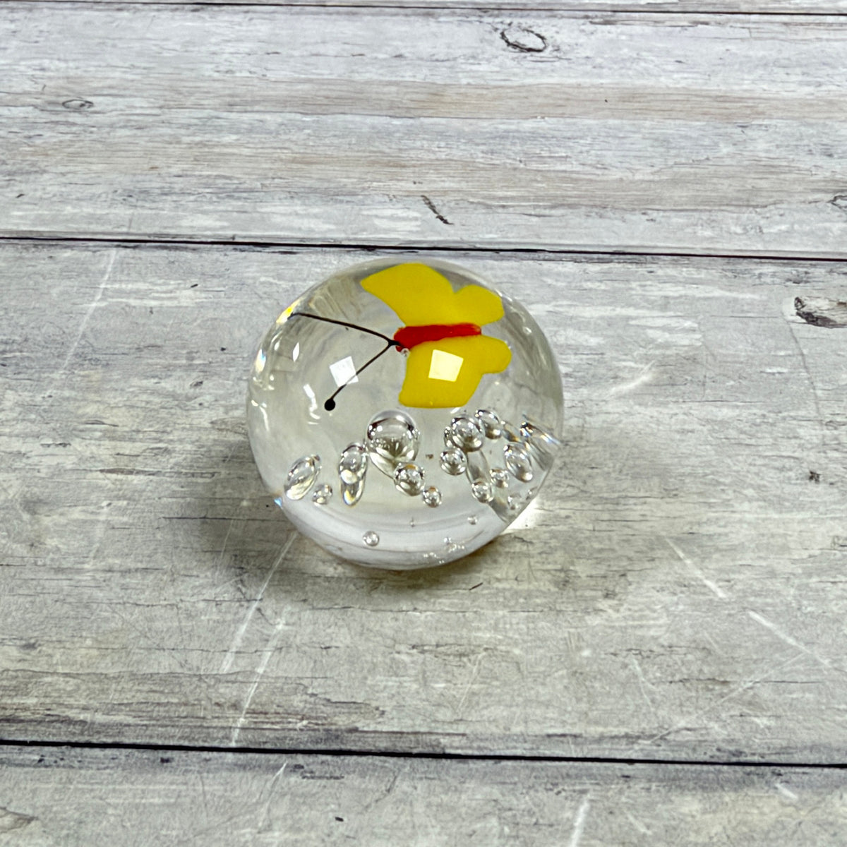 Mini clear glass paperweight with a yellow butterfly, red body, black antennae and controlled bubbles