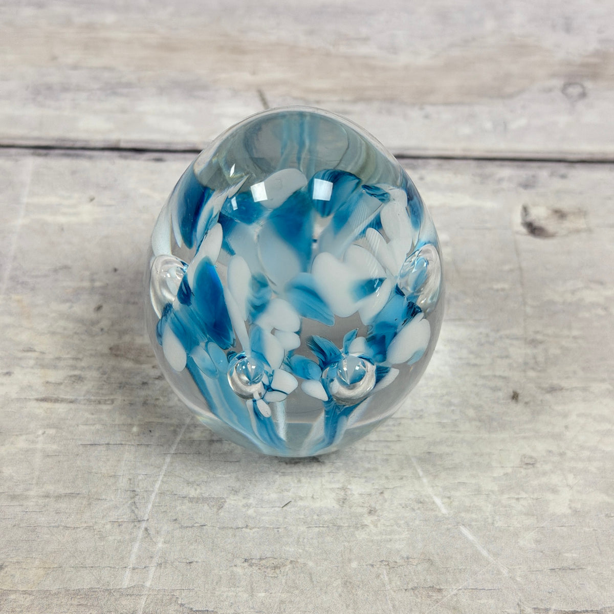 Angled view of blue and white floral decoration and suspended bubbles in a Gibson glass egg paperweight